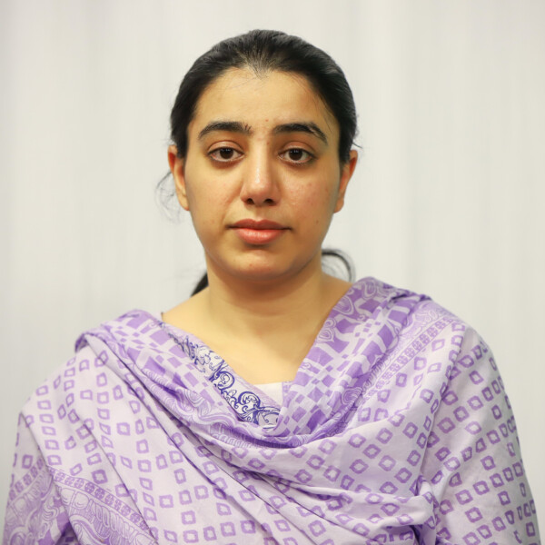 Portrait of a woman with dark hair tied back, wearing a lavender patterned scarf, looking straight at the camera with a neutral expression.